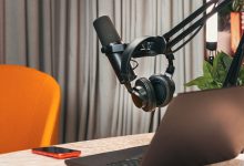 Estúdio de podcast com microfone, fones de ouvido, laptop e smartphone sobre uma mesa de madeira