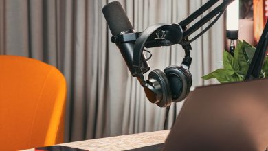 Estúdio de podcast com microfone, fones de ouvido, laptop e smartphone sobre uma mesa de madeira