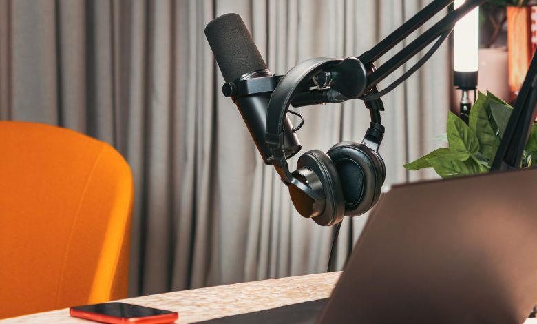 Estúdio de podcast com microfone, fones de ouvido, laptop e smartphone sobre uma mesa de madeira