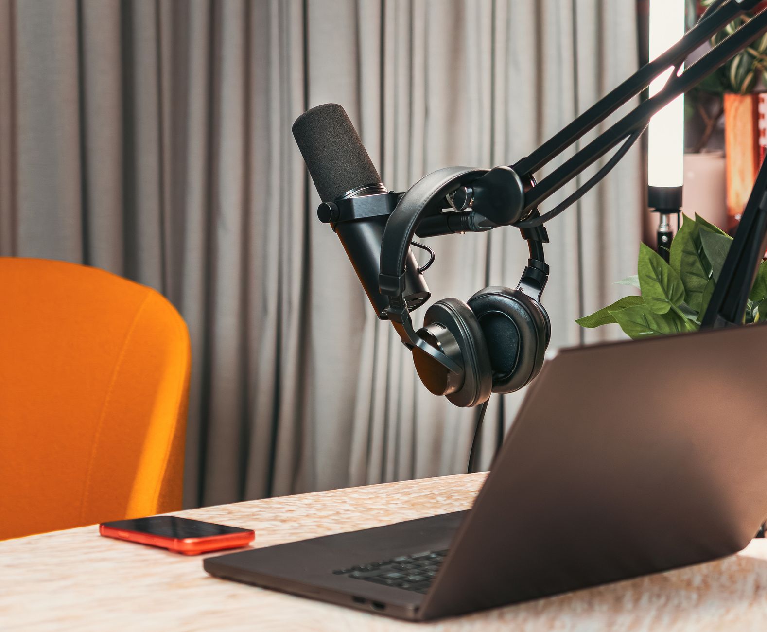 Estúdio de podcast com microfone, fones de ouvido, laptop e smartphone sobre uma mesa de madeira