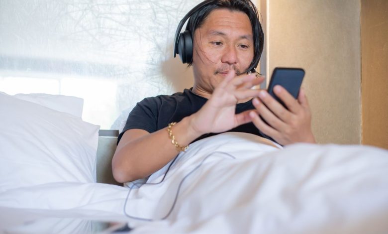 Homem asiático usando smartphone e fones de ouvido em um quarto aconchegante.
