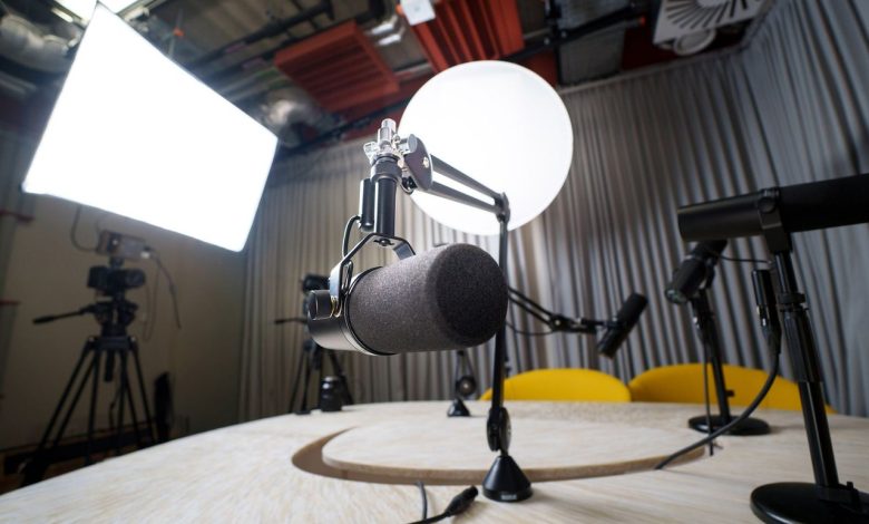 Estúdio moderno de podcast com microfones, cadeiras e equipamentos de iluminação.