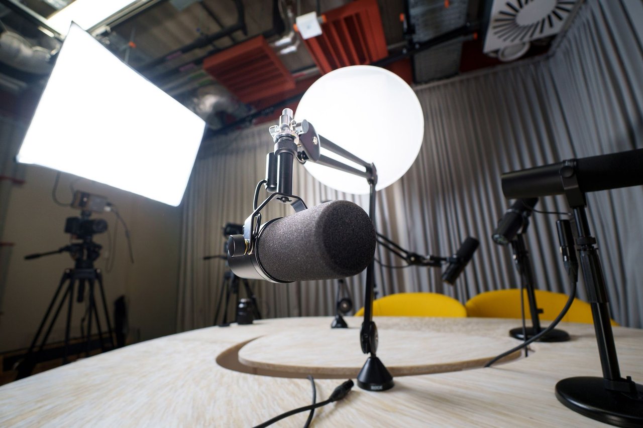 Estúdio moderno de podcast com microfones, cadeiras e equipamentos de iluminação.