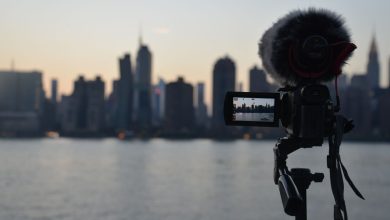Câmera com microfone diante da paisagem de Nova York ao amanhecer, vista a partir da margem de um rio.