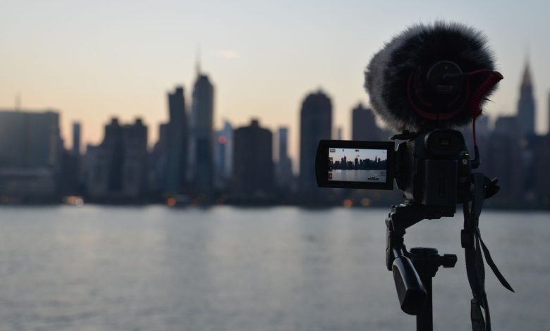 Câmera com microfone diante da paisagem de Nova York ao amanhecer, vista a partir da margem de um rio.